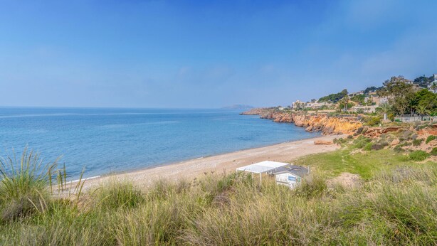 Una playa costera con vistas claras al mar, una orilla arenosa y un edificio con techo blanco.