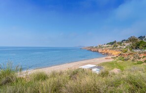 Une plage côtière offrant une vue dégagée sur la mer, une rive sablonneuse et un bâtiment doté d’un toit blanc.