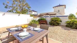 Un patio exterior con una mesa dispuesta para comer, rodeado de plantas y un edificio con tejado de azulejos.