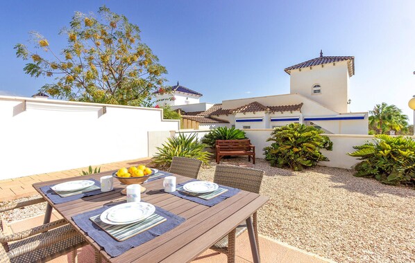 Un patio exterior con una mesa dispuesta para comer, rodeado de plantas y un edificio con tejado de azulejos.
