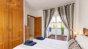 Habitación de hotel con una cama grande, armario de madera y un balcón con cortinas.