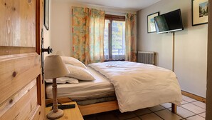 A bedroom with a bed, a bedside table with a lamp, a TV mounted on the wall, and a window with curtains. - Clos 22 - appartement - 10 pers - proche centre (Les Gets)