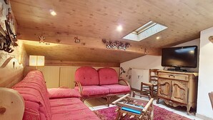 A cozy cabin interior with a wooden ceiling, a sofa with patterned cushions, a television, and a wooden cabinet. - Clos 28 - appartement - 6pers - proche centre (Les Gets)