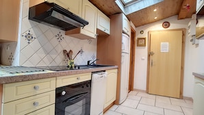 A compact kitchen with a stove, oven, sink, and a wooden ceiling. - Clos 28 - appartement - 6pers - proche centre (Les Gets)