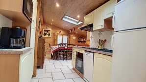 A compact kitchen with wooden cabinets, a dining table with chairs, and a built-in oven. - Clos 28 - appartement - 6pers - proche centre (Les Gets)