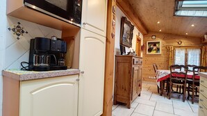 A kitchen with a coffee maker, wooden cabinets, a dining table with chairs, and a painting on the wall. - Clos 28 - appartement - 6pers - proche centre (Les Gets)