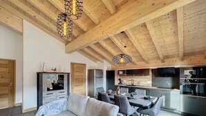 Una cocina moderna con electrodomésticos de acero inoxidable, un comedor con sofá y sillas grises, y vigas de madera en el techo.