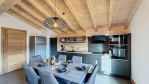 Una cocina moderna con comedor, vigas de madera en el techo y una isla central con estufa integrada.