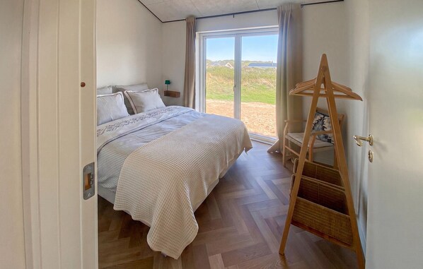 A bedroom with a bed, a wooden ladder, and a view of the outdoors through a large window.