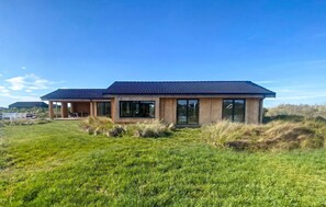 A modern house with a large glass door, a covered outdoor area, and a grassy field in the foreground.
