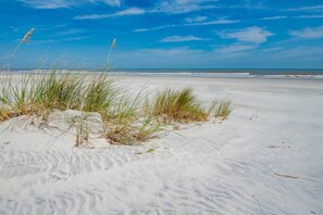 A sandy beach with grass and a clear blue sky.