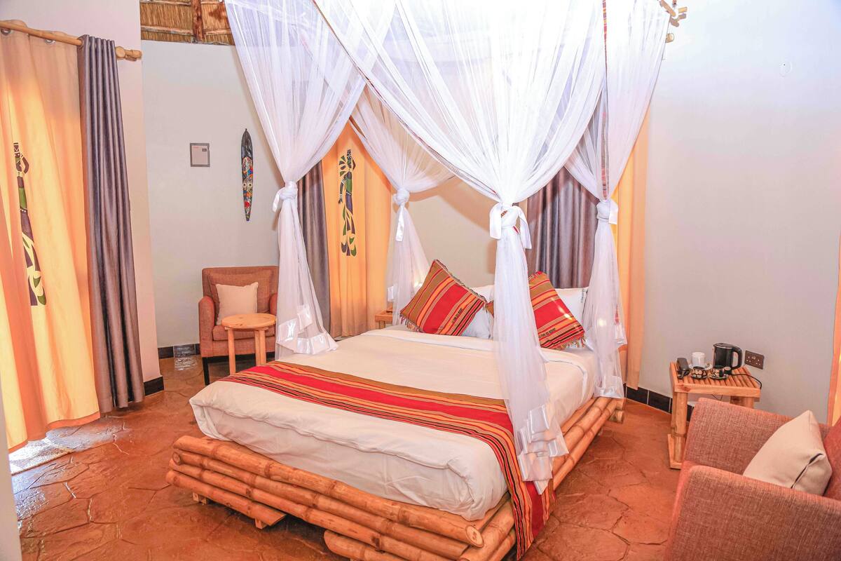 A room with a four-poster bed, a small wooden table with a coffee pot, and a chair.