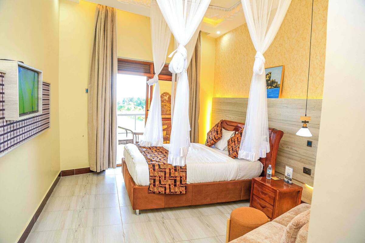 A spacious bedroom with a large bed, a bedside table, a nightstand, and a view of the outdoors.