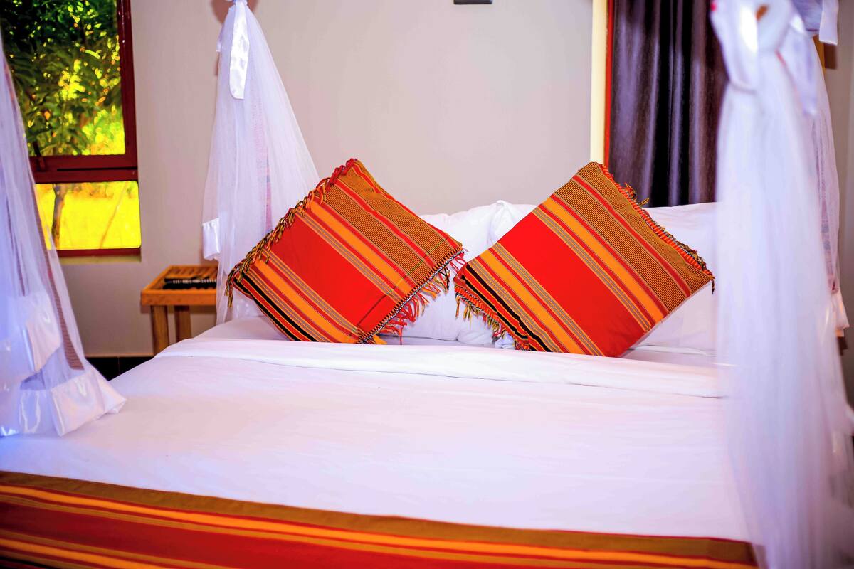 A bed with white linens and two colorful pillows, a bedside table, and a window with curtains.