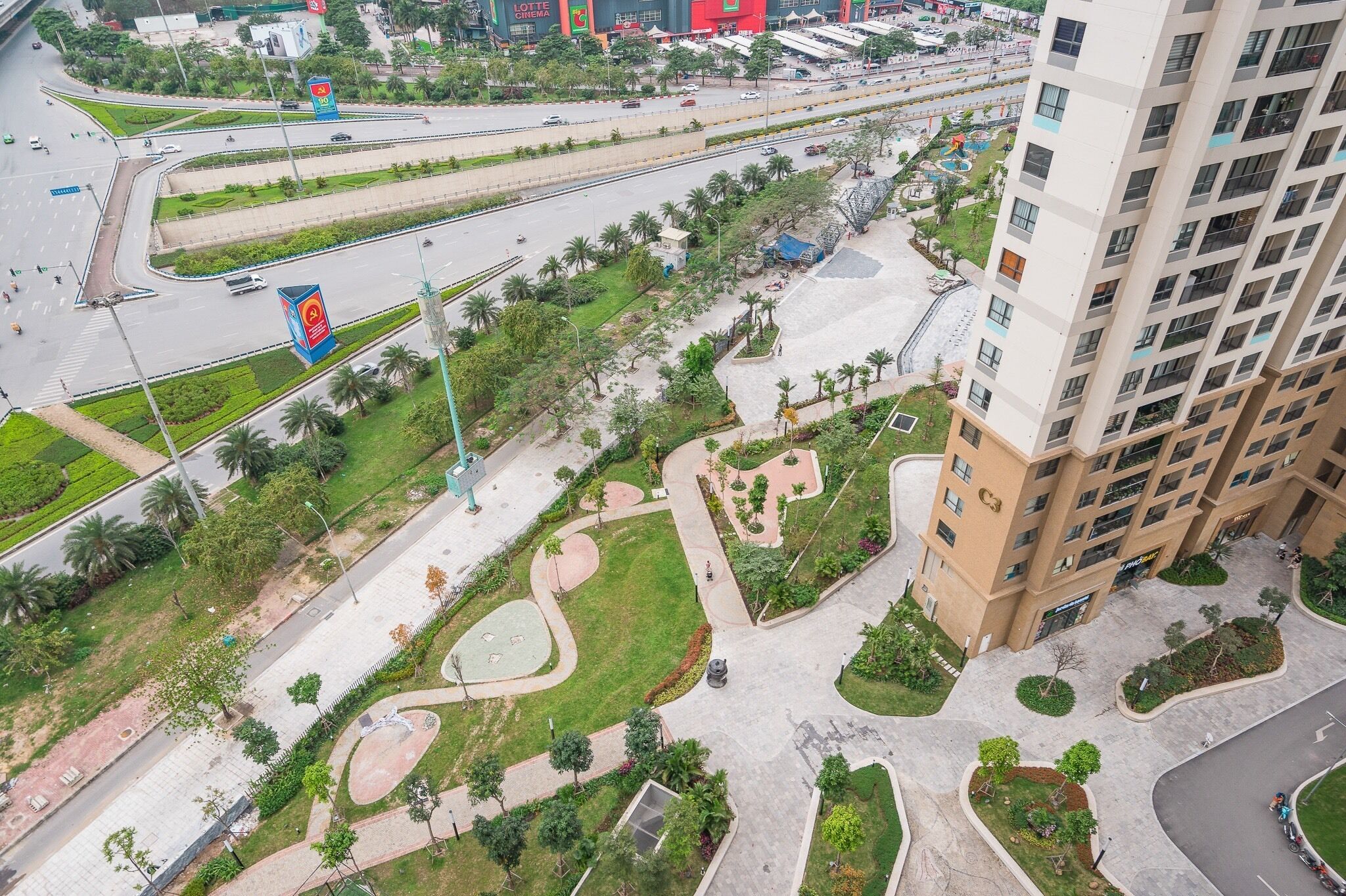 Vue aérienne d’un quartier urbain moderne, avec un parking à plusieurs niveaux, des espaces piétonniers aménagés et un immeuble de grande hauteur abritant des commerces.