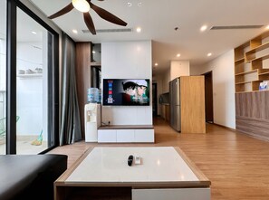 A modern living room with a TV, a water dispenser, and a ceiling fan. - SOL - Vinhomes D'capital (Hanoi)