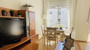 A modern living room with a flat-screen TV, wooden furniture, a glass coffee table, and a view of a building through a window.