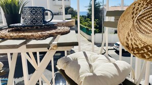 A balcony with a woven mat, a white cushion, a woven hat, a patterned mug, and a potted plant.
