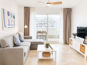 Un soggiorno moderno con divano, tavolino, televisore e un balcone con vista sulla città.