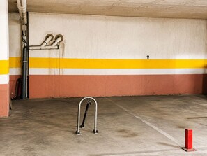 Un parcheggio sotterraneo con pavimento in cemento, pareti a strisce gialle e bianche e un parcometro in metallo.