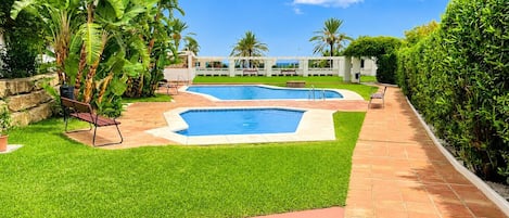 A swimming pool area with two pools, surrounded by well-maintained grass and a brick pathway.