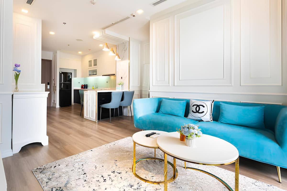 A modern living room with a blue sofa, two round tables, and a kitchen in the background.