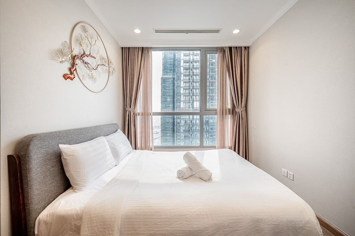 A hotel room with a large bed, a window with curtains, and a wall-mounted artwork.