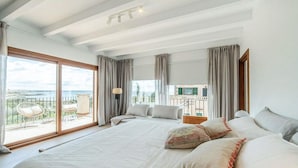 A spacious bedroom with a large bed, a balcony with a view, and a separate seating area with a table and chairs. - Stunning home in Llucmajor with private swimming pool, can be inside or outside (Llucmajor)