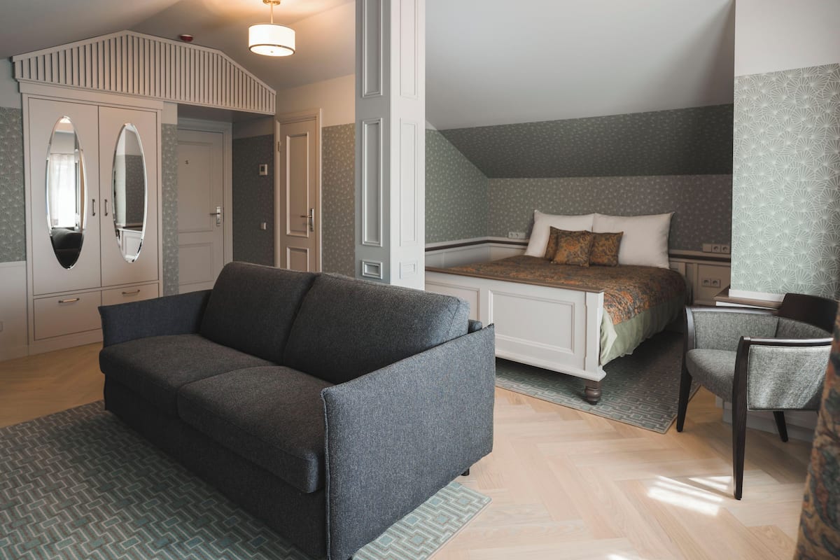 Une chambre à coucher avec un lit, un canapé gris, une chaise, une armoire et un miroir.