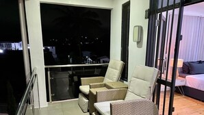 A balcony with wicker furniture, a glass door, and a view of the night cityscape. - 3 Bedroom Apartment in Suva (Suva)