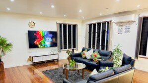 A modern living room with a black leather sofa, a glass coffee table, and a flat-screen TV. - 3 Bedroom Apartment in Suva (Suva)