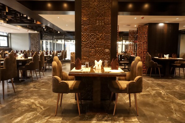 Un comedor amplio con varias mesas y sillas, con un diseño moderno y una pared decorativa central.