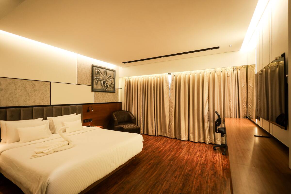 A hotel room with a large bed, a desk, a chair, a television, and a window with curtains.