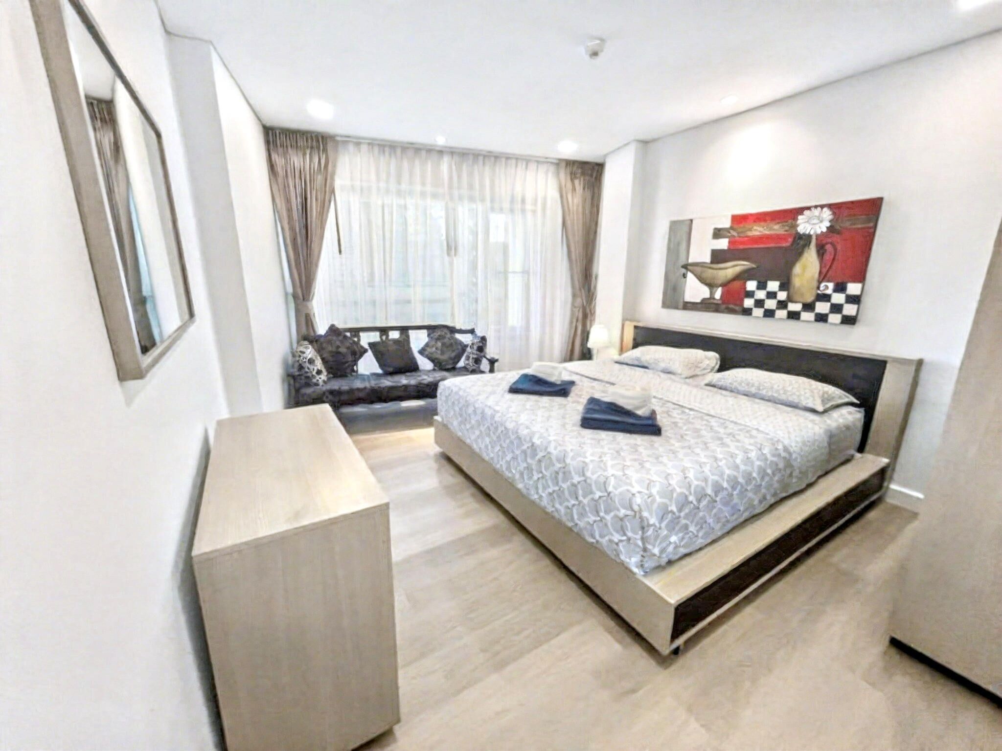 A modern bedroom with a large bed, a bench, and a painting on the wall.