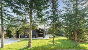 Ein modernes Haus mit großer Terrasse, umgeben von Bäumen und einem gepflegten Rasen.