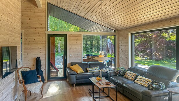 Ein modernes Wohnzimmer mit Holzwänden, einem großen Sofa, einem Couchtisch und Blick ins Freie.