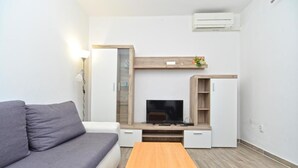 A modern living room with a grey sofa, a wooden coffee table, a TV, and built-in storage units. - Charming coastal gateway (Fažana)