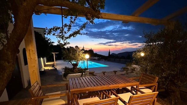 Une terrasse extérieure avec une table et des chaises en bois, une piscine et une vue sur le coucher de soleil.