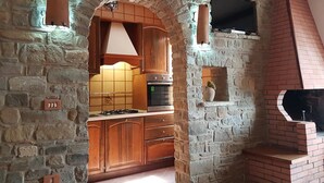 Une cuisine avec des murs en pierre, des meubles en bois, une cuisinière à gaz et un four en briques.