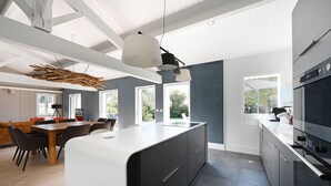 Una cocina moderna con una isla central, ventanas amplias y un comedor con una mesa y sillas de madera.