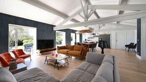 Amplia sala de estar con un sofá grande, una mesa de centro y un televisor. Se observa un comedor con sillas y una mesa al fondo.