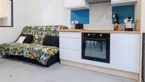 A compact kitchen with a built-in oven and a small dining area with a sofa.