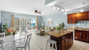 Una cocina moderna con armarios de madera, una isla central y un comedor con sillas blancas y una mesa.
