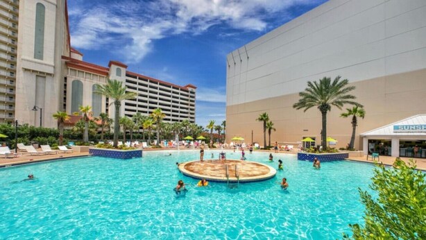 Una gran piscina al aire libre rodeada de palmeras y sillas de descanso, con un edificio de hotel al fondo.