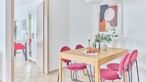 A dining area with a wooden table, six pink chairs, a white pendant light, and a painting on the wall. - Rosalia - Stylish living, central experience (Kaiserslautern)