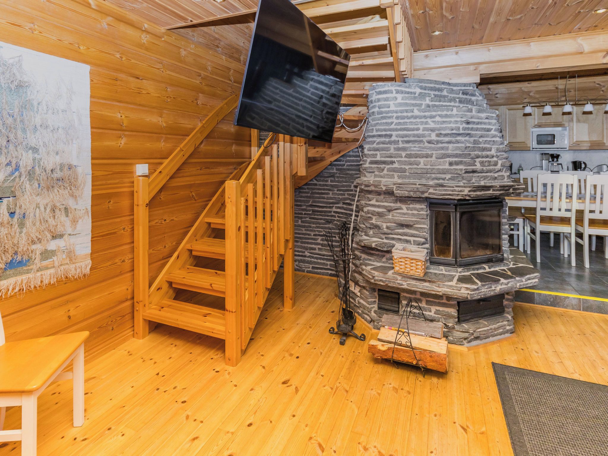 A wooden interior with a stone fireplace, a wooden staircase, and a television mounted on the wall.
