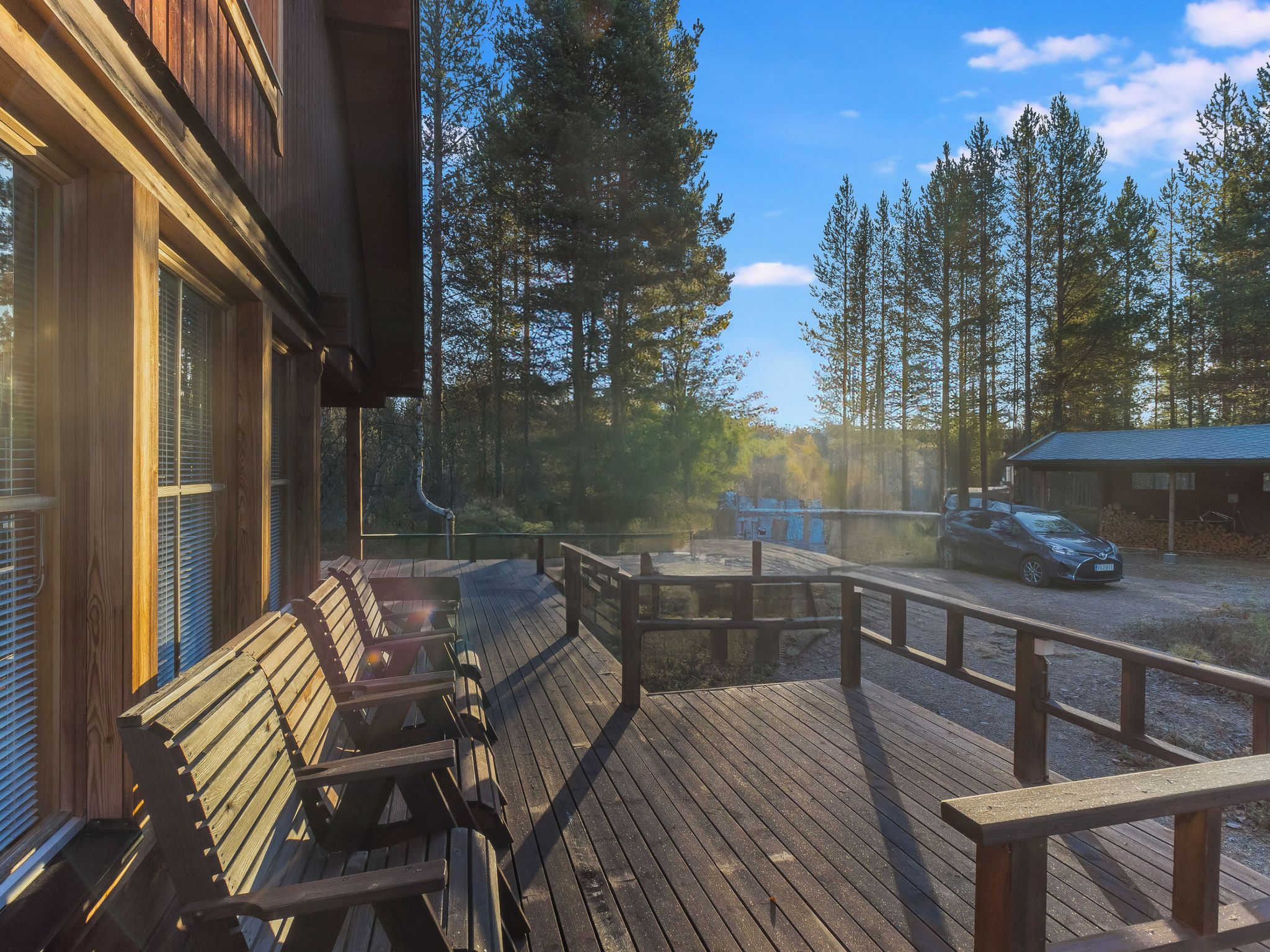 Une terrasse en bois avec des bancs, une vue sur une forêt et un bâtiment en arrière-plan.
