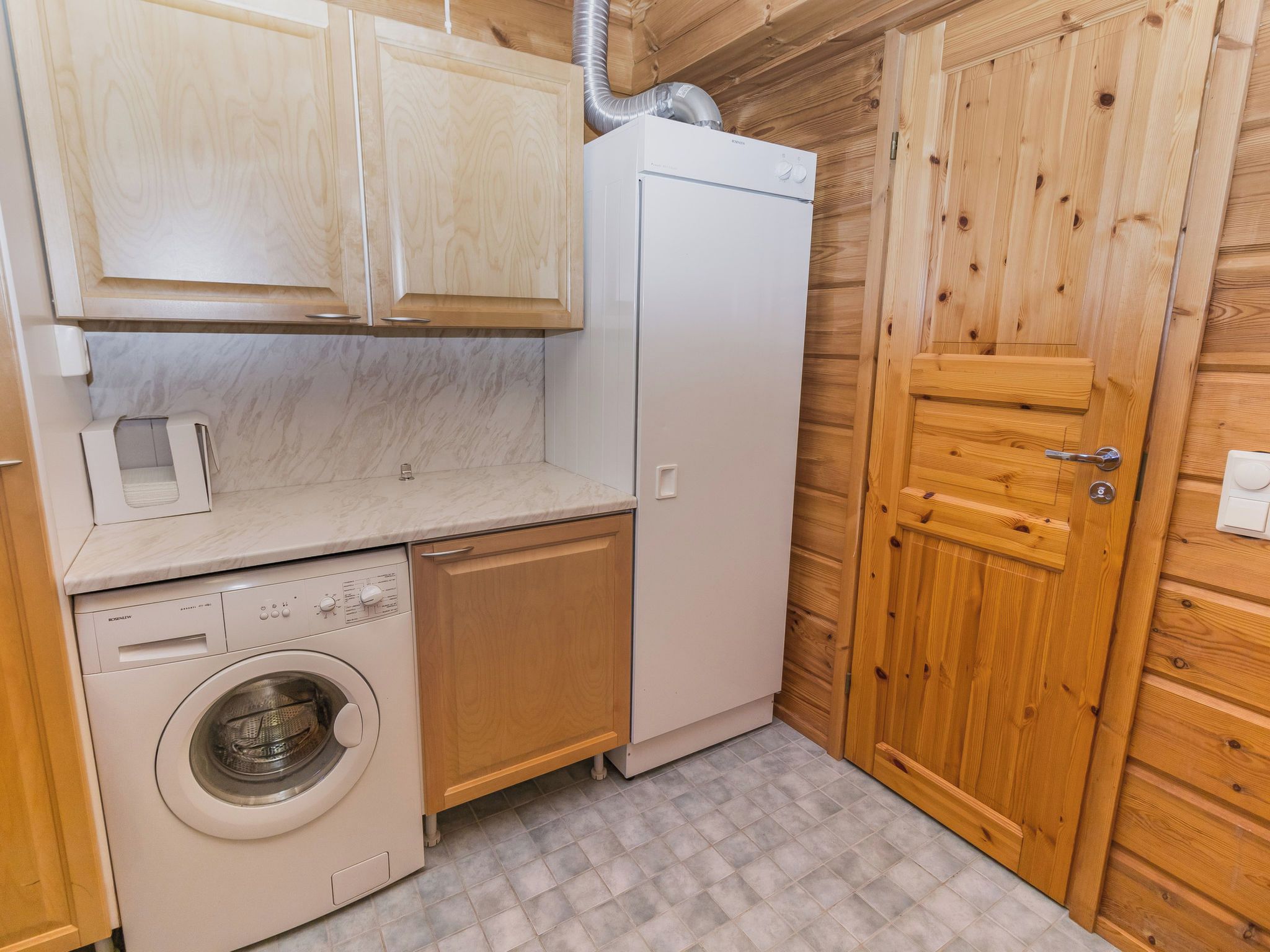 A compact kitchen with a washing machine, a refrigerator, and wooden cabinets.