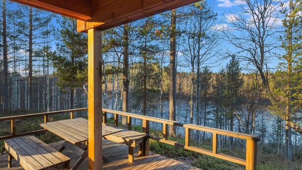 A wooden deck with picnic tables overlooking a forested area and a body of water. - Alakoski by Interhome (Inari)