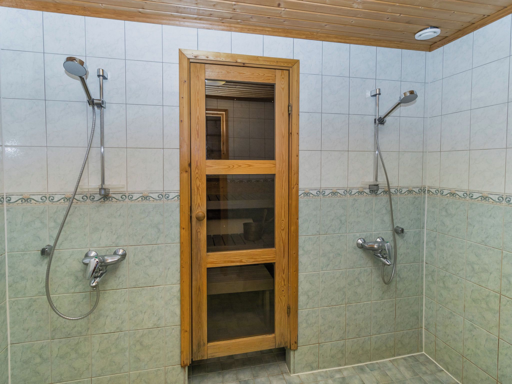 A bathroom with two showerheads, a wooden door, and tiled walls.